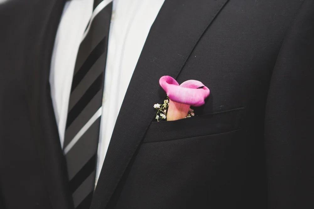 Close-up of a bright pink boutonniere pinned to a black suit jacket.