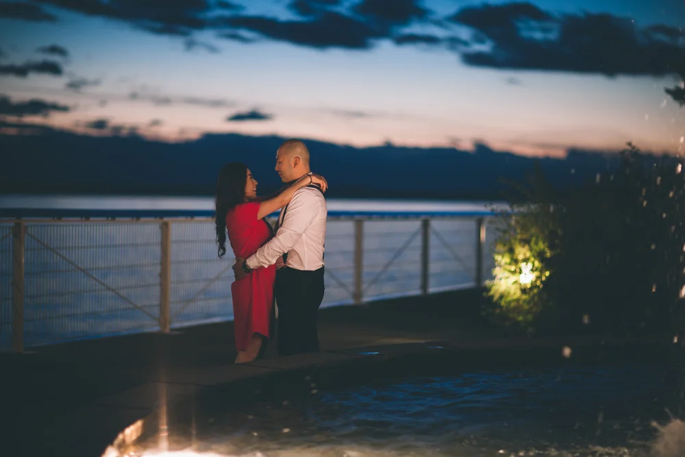 Couple embracing on a waterfront terrace at dusk.
