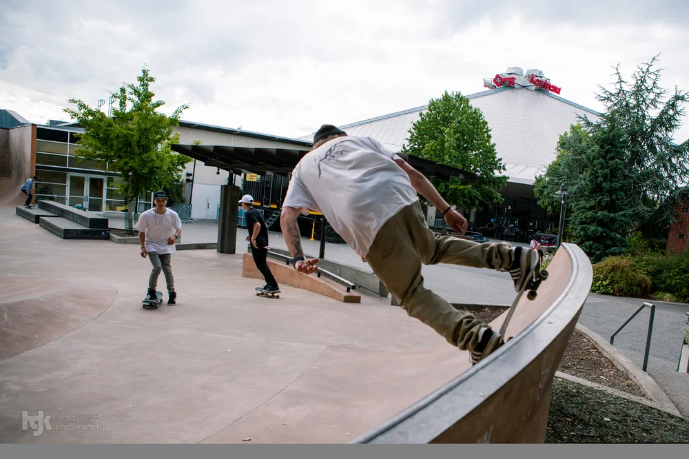 Skateboarder riding along the edge of a concrete ledge while other skaters watch.