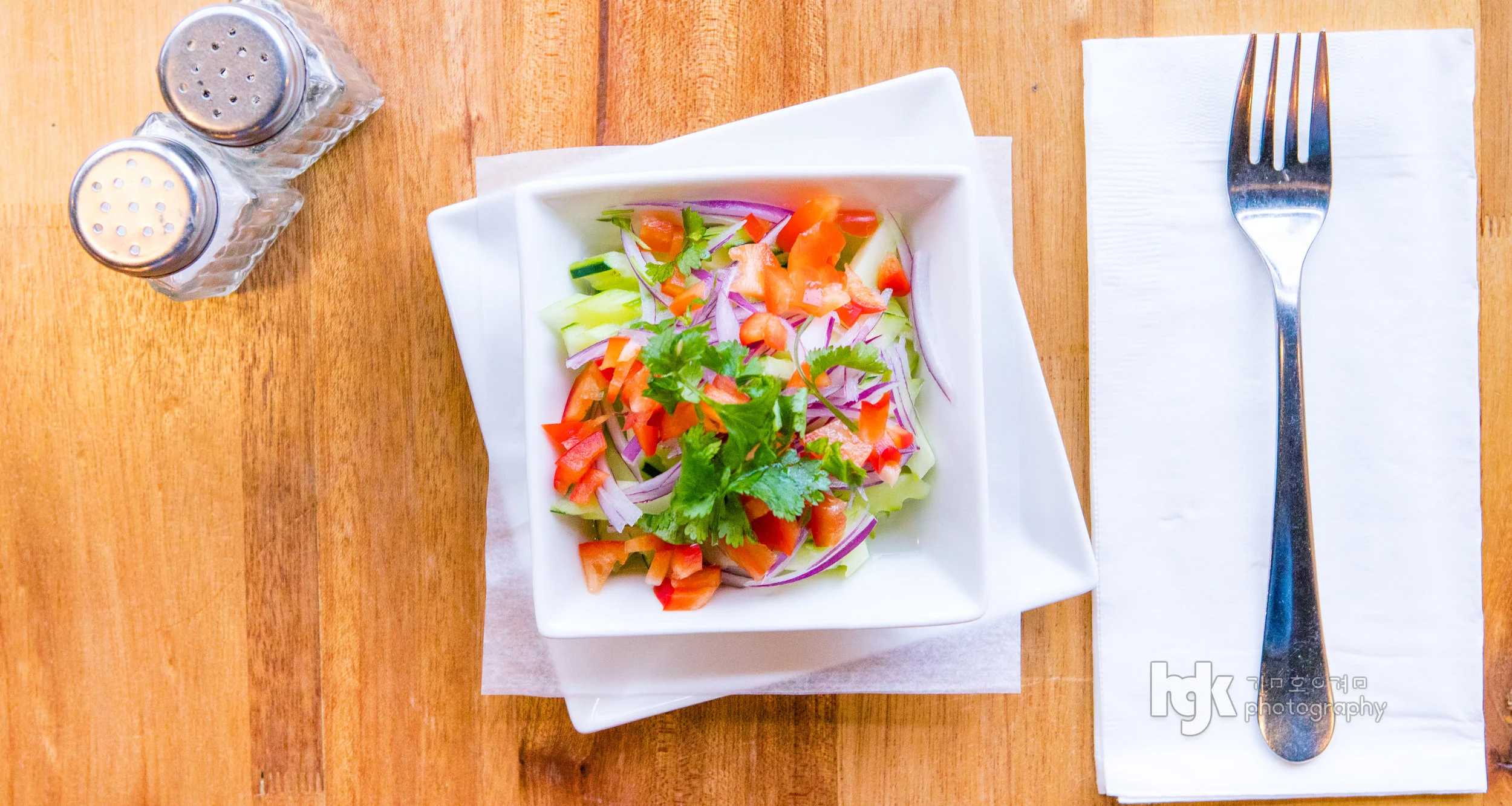 Overhead food photograph of a fresh salad with tomatoes and herbs on a square white plate.