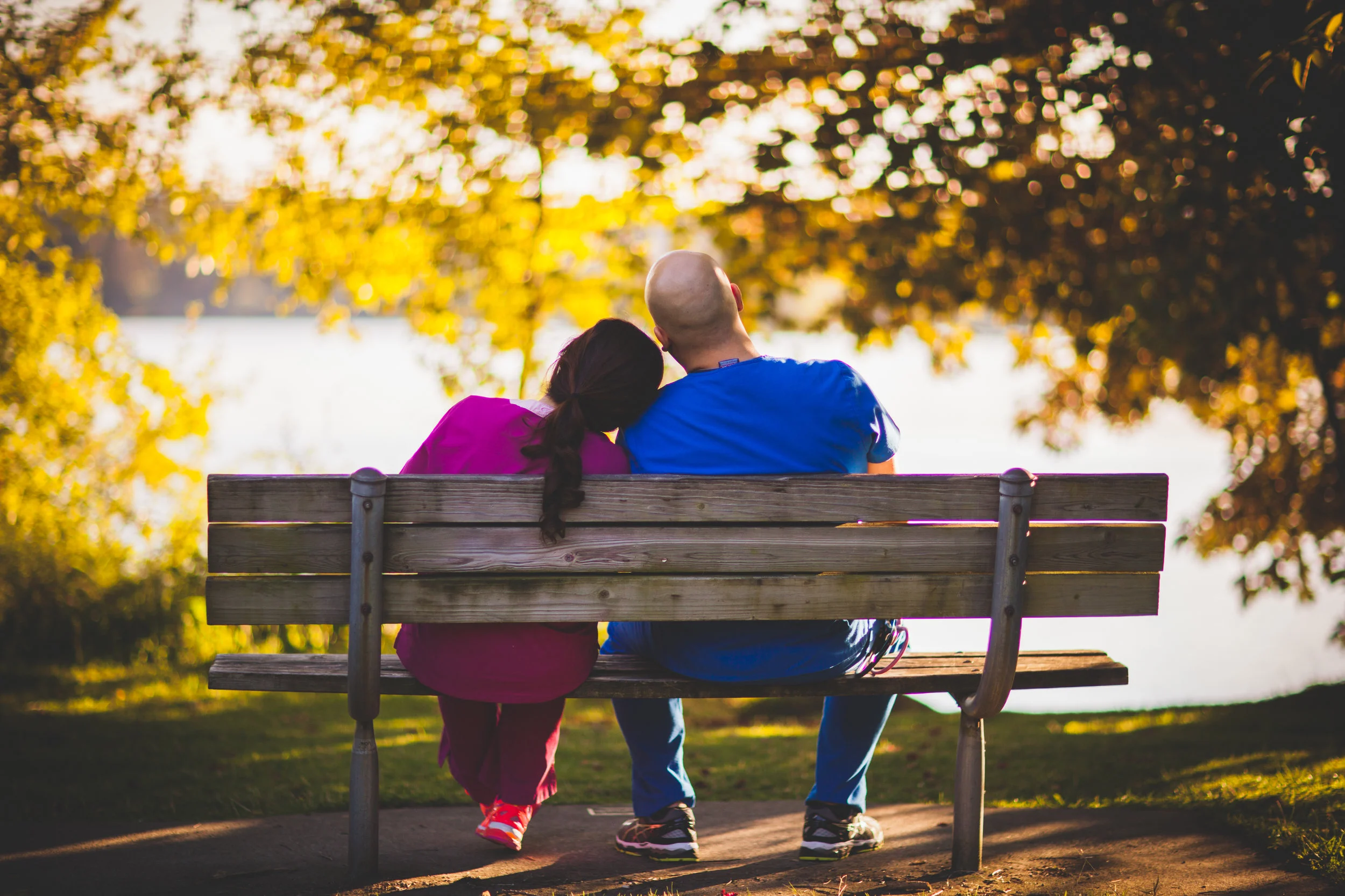 Couple sitting together on a park bench under warm autumn light.