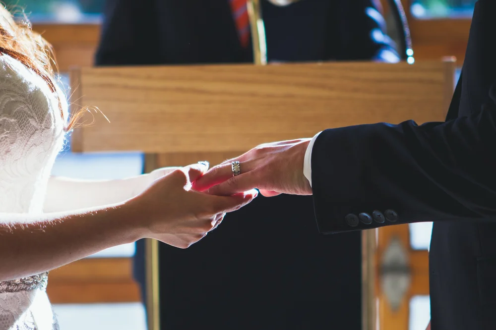 Close view of a couple's hands meeting during a wedding ring exchange.