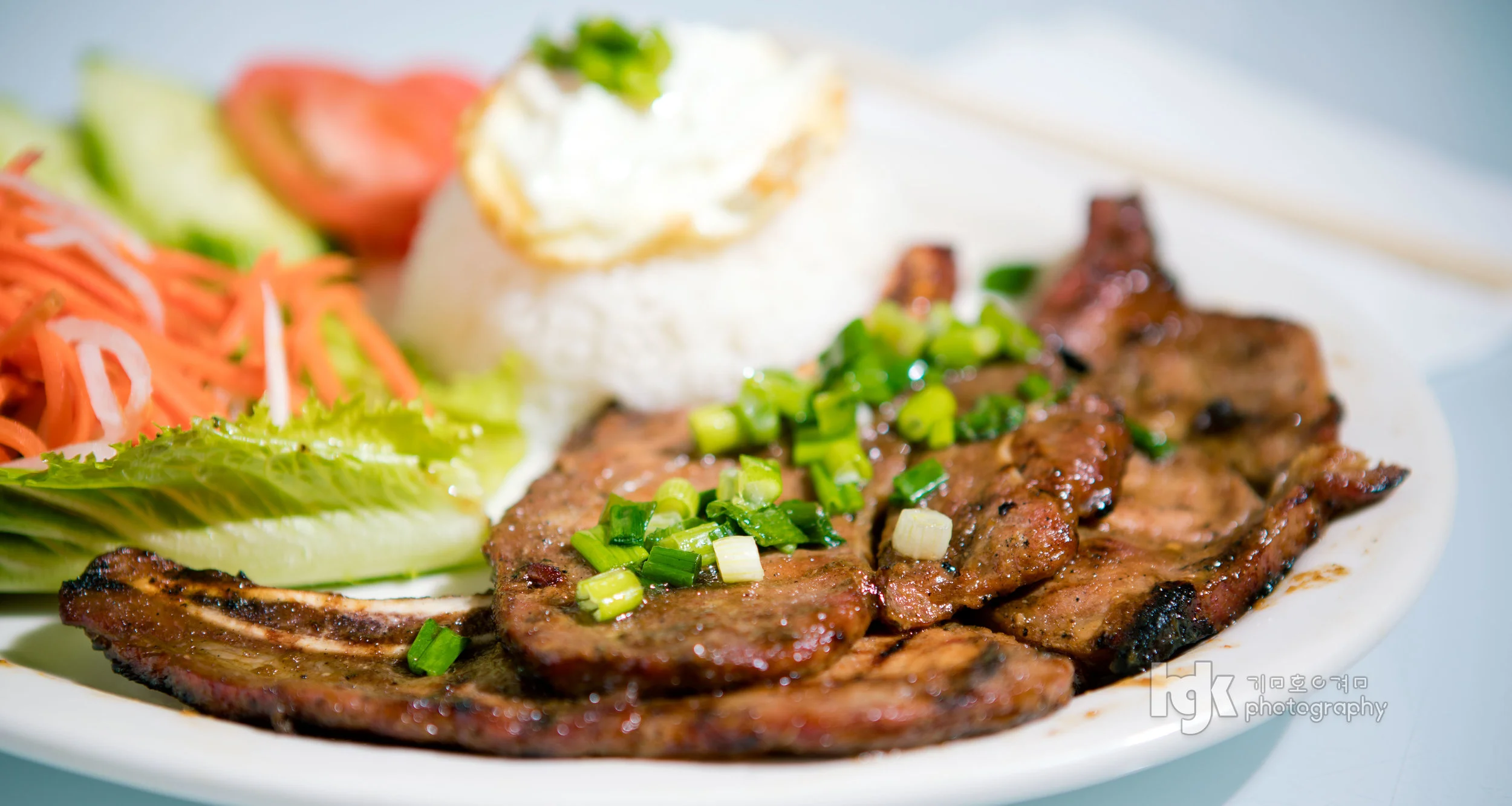 Grilled meat plate with rice, lettuce, pickled vegetables and scallions.