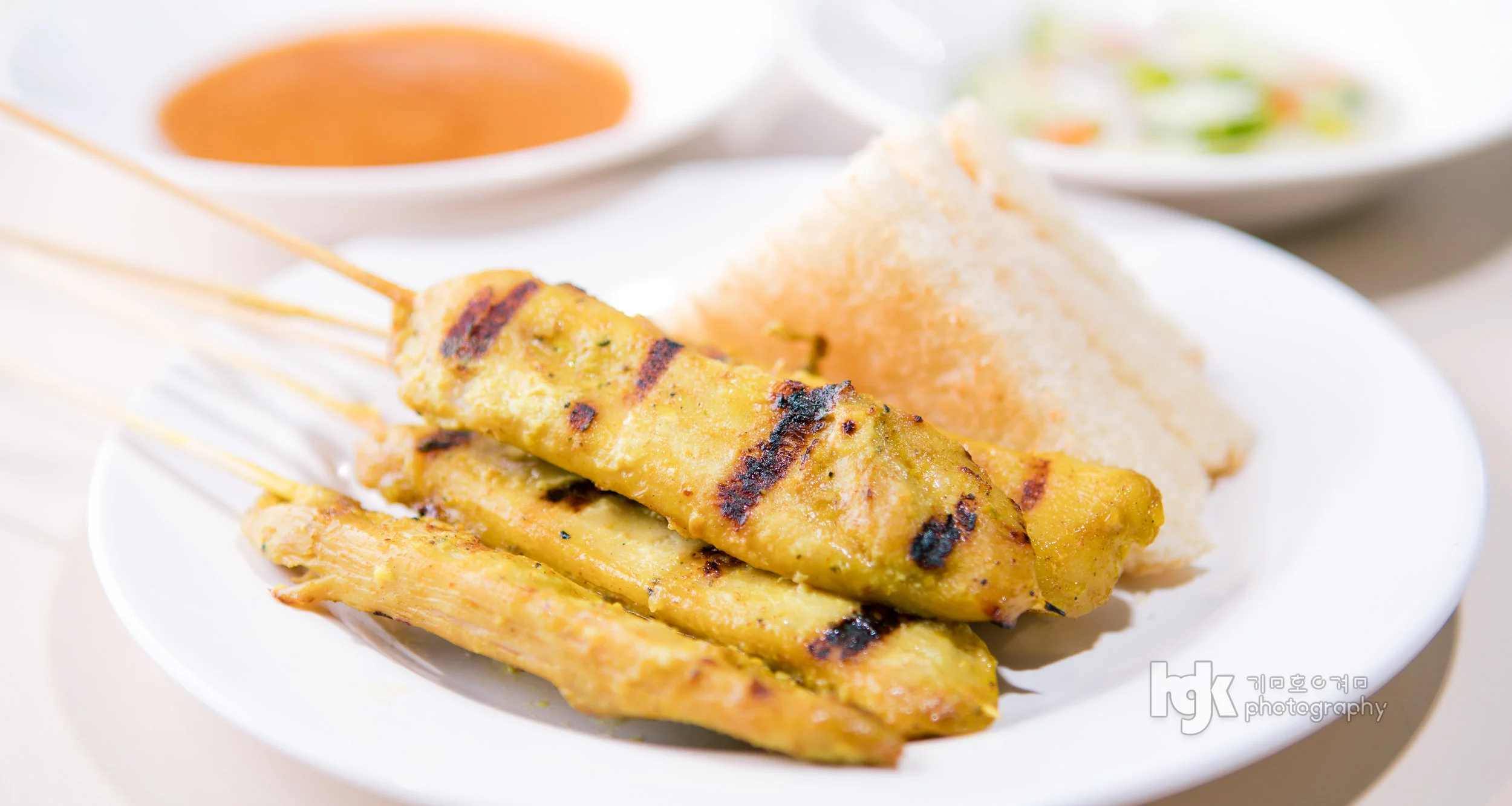 Grilled satay skewers served with toast and dipping sauce on a white plate.
