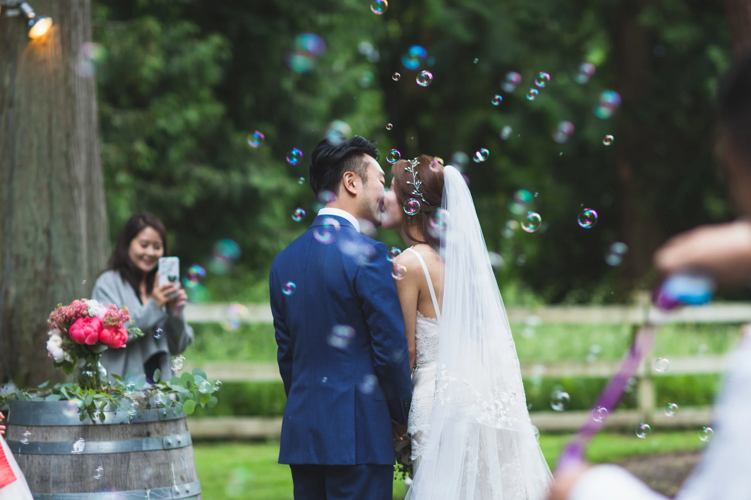 Bride and groom kissing outdoors as bubbles float around them.