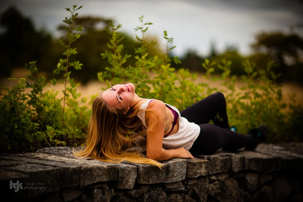 Model reclining along a low stone wall with long hair falling toward the camera.