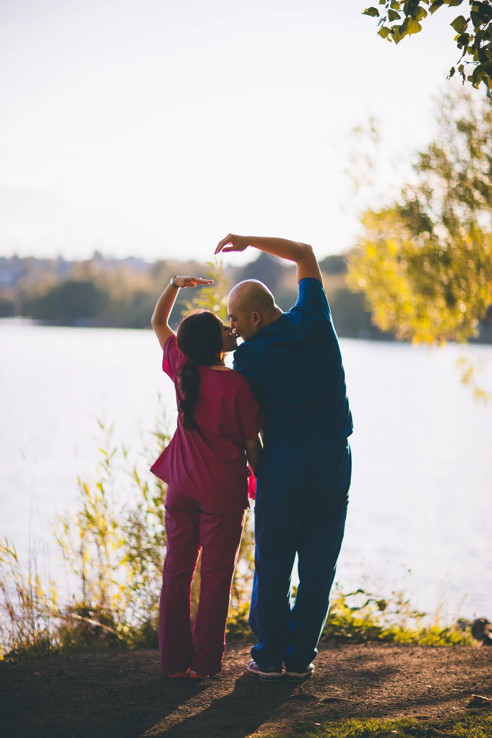 Couple raising their arms together beside a lake in warm autumn light.