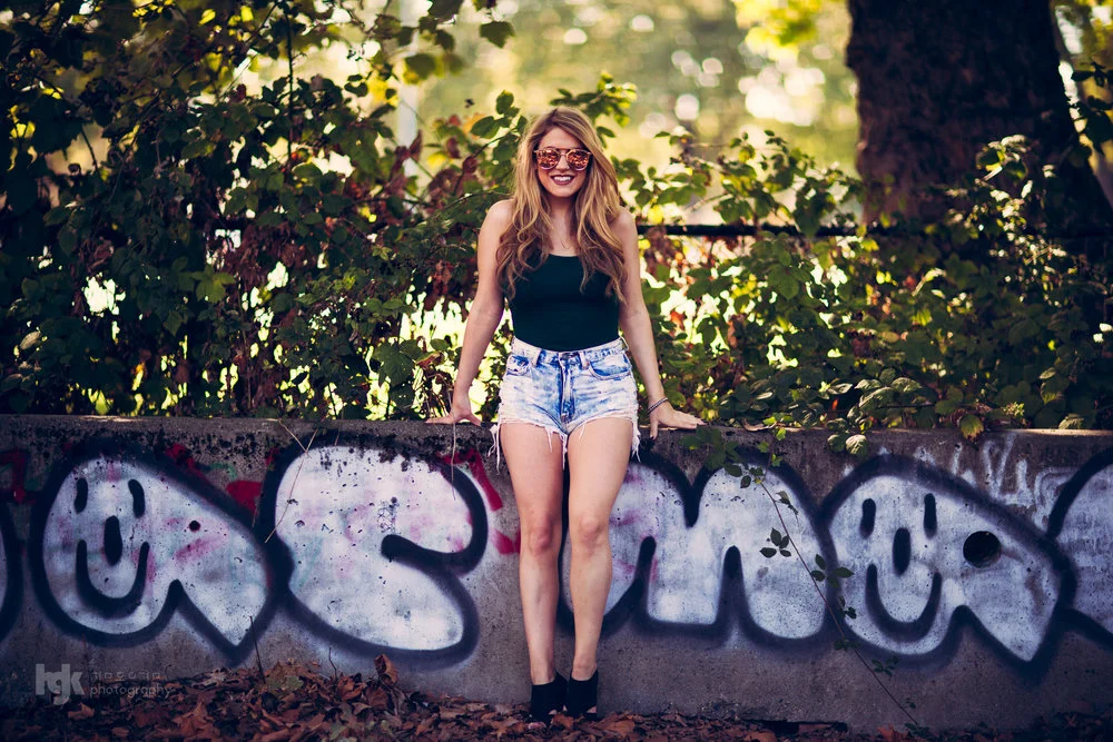 Model standing in front of large graffiti lettering in warm backlight.