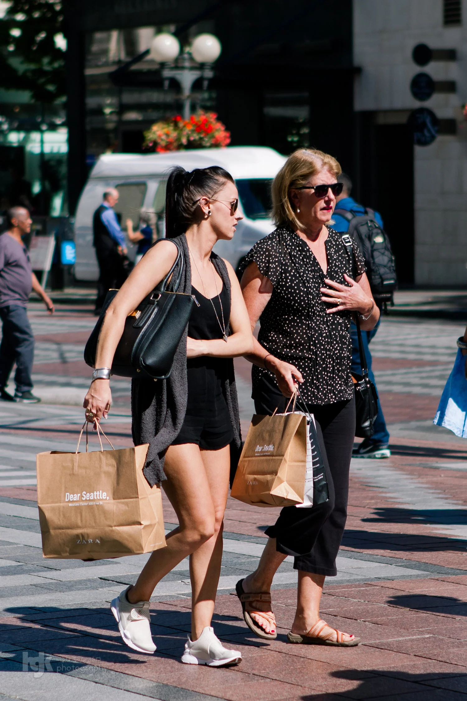 Two shoppers walking through downtown Seattle carrying paper bags.