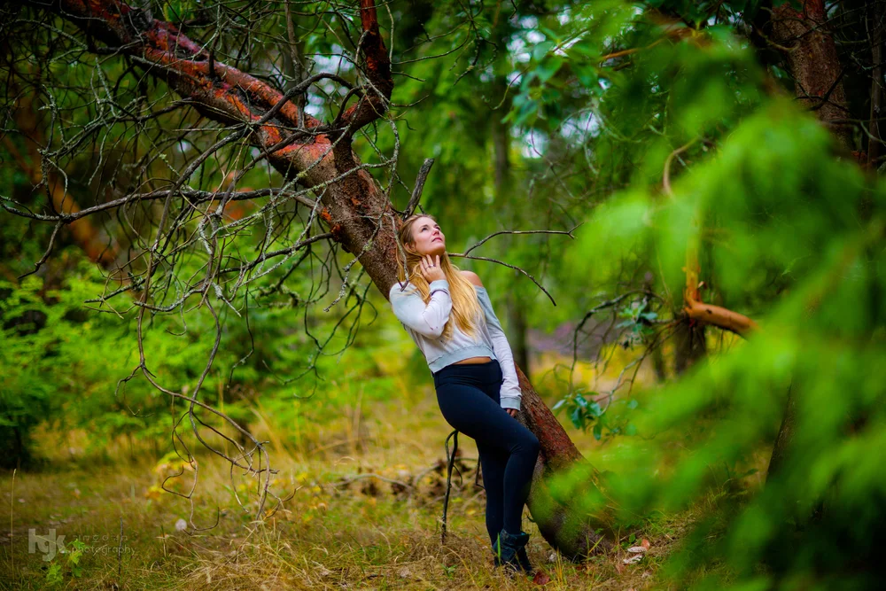 Model reaching into hanging tree branches in a dense green setting.