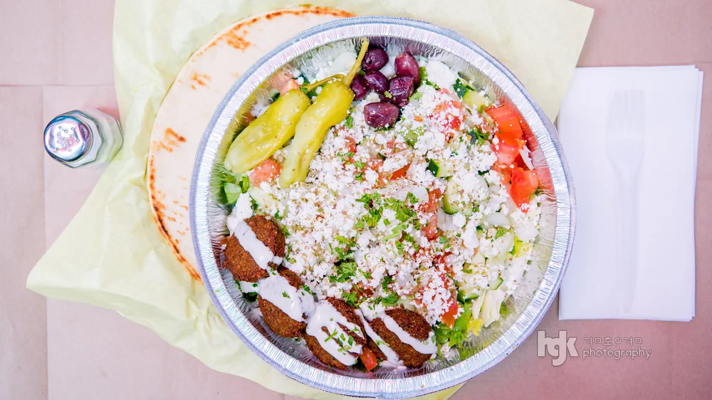 Overhead platter with salad greens, feta, olives, tomato, peppers and sliced meat.